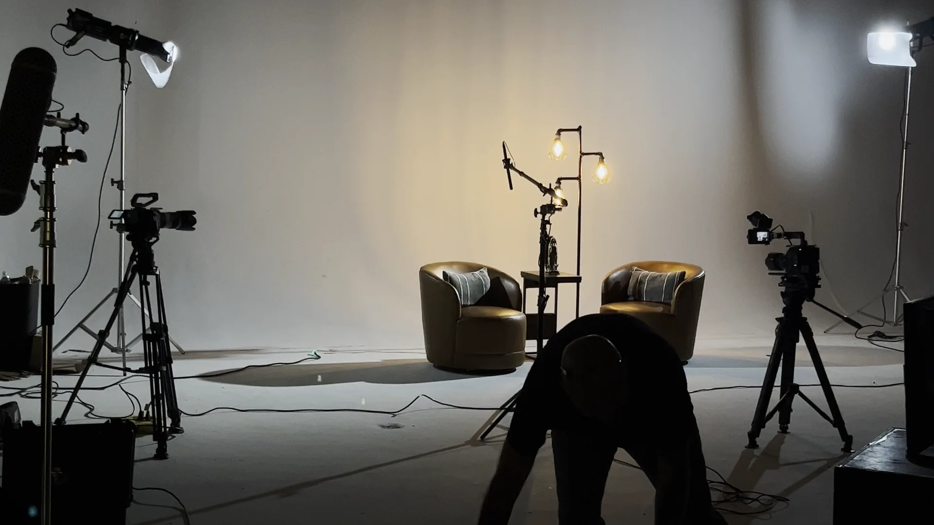 Crew member reaching for gear on the interview set, with two cameras and a boom microphone visible