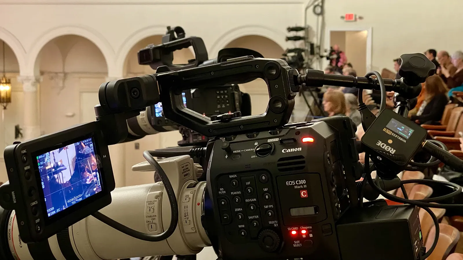 Behind-the-scenes camera view of a Tampa Bay Symphony performance, with a Canon C300 Mark III in the foreground, its tally light active, and musicians visible on the monitor and beyond.